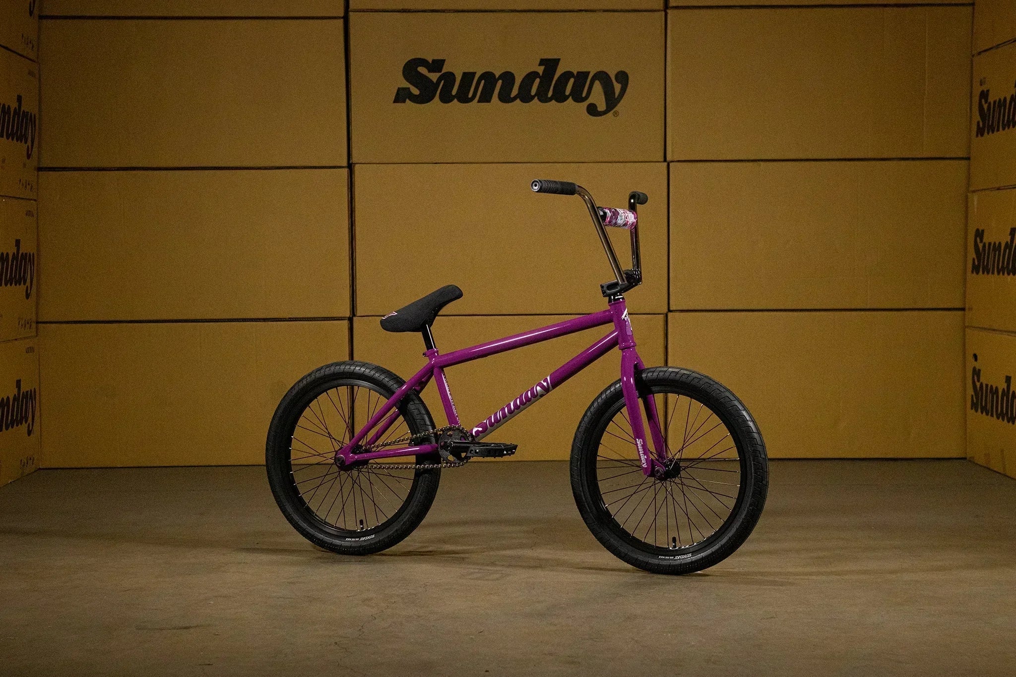 Vélo BMX Sunday violet avec cadre et fourche assortis devant des cartons de marque.