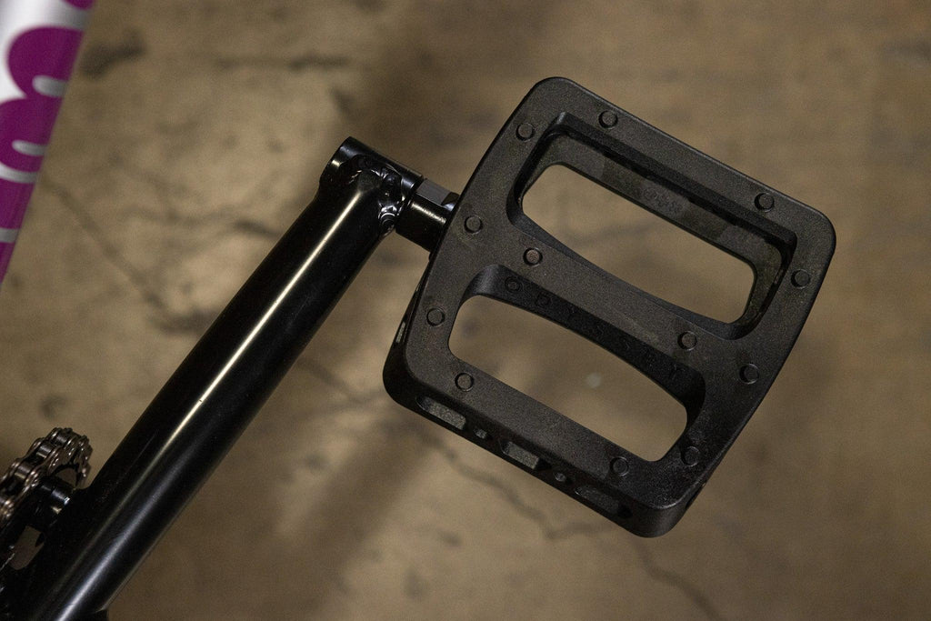 Gros plan d'une pédale de vélo BMX en nylon noir fixée à une manivelle.