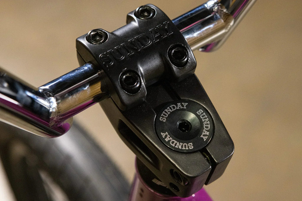 Gros plan d'une potence de vélo BMX noire de marque Sunday avec guidon chromé.