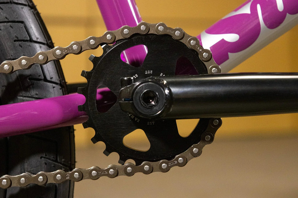 Gros plan d'un plateau noir et d'une chaîne sur un cadre de vélo BMX violet.
