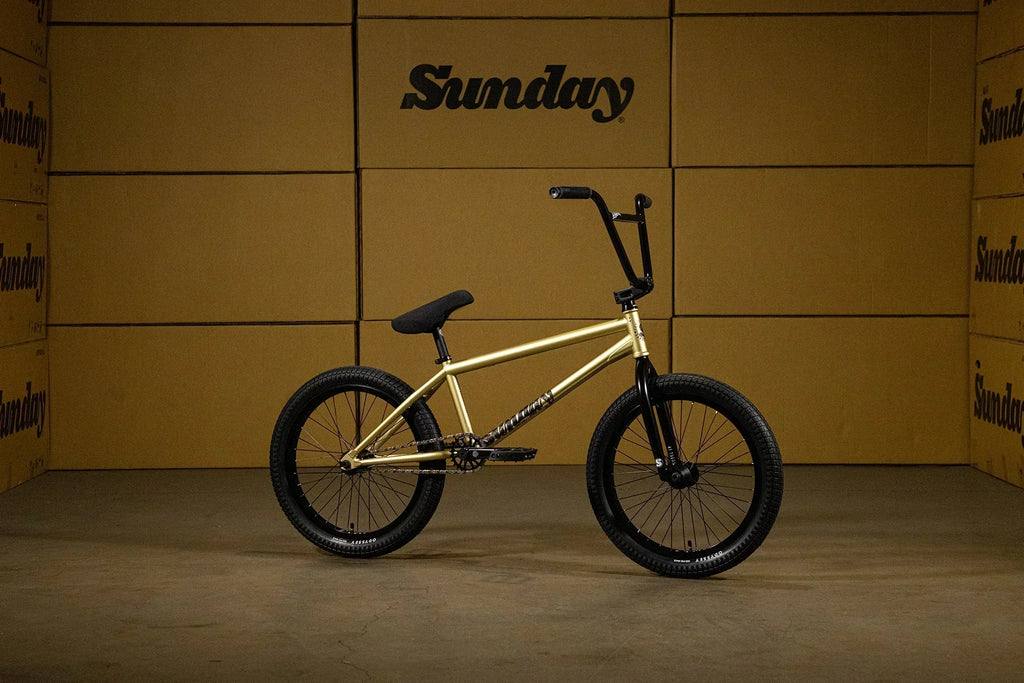Vélo BMX Sunday doré avec pneus noirs sur fond de cartons de rangement