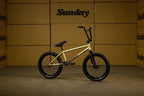 Vélo BMX Sunday doré avec pneus noirs sur fond de cartons de rangement
