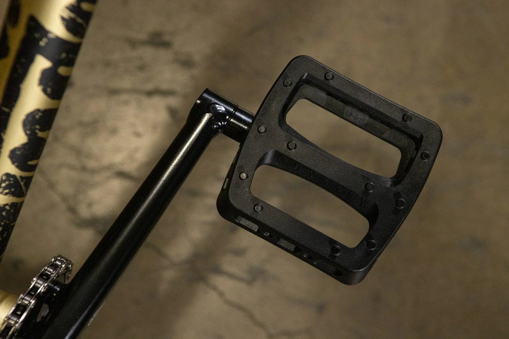 Gros plan d'une pédale de vélo BMX noire fixée à une manivelle.
