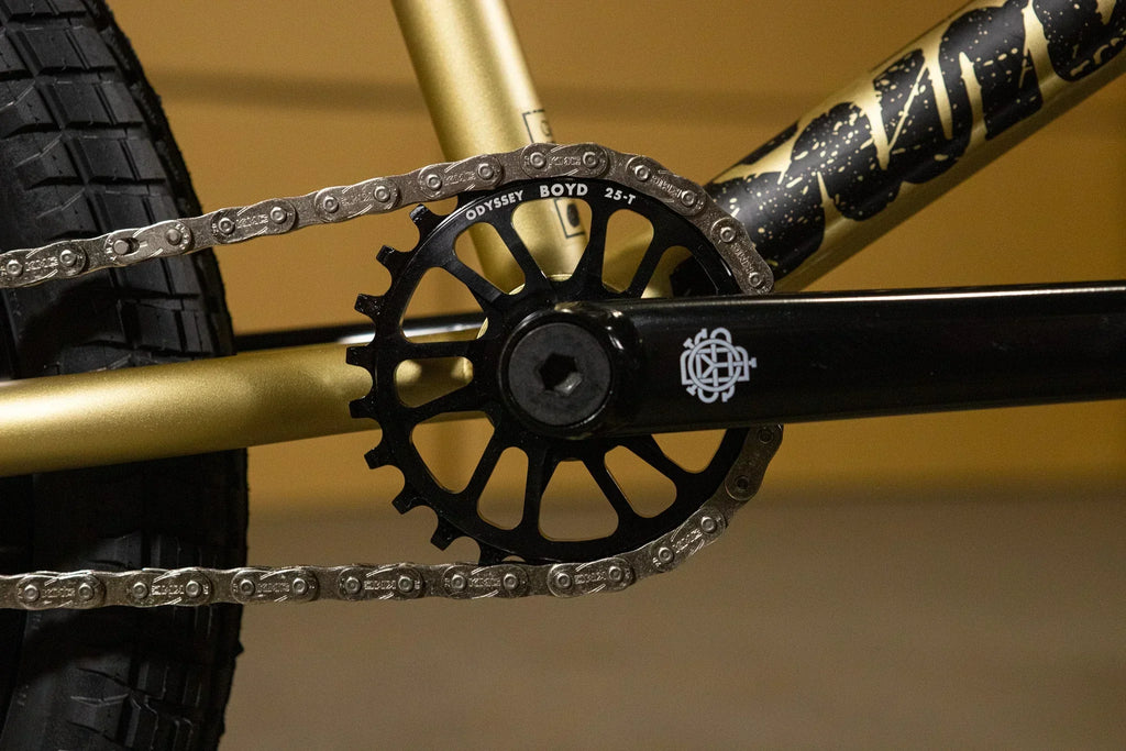 Gros plan d'un plateau Odyssey Boyd 25T et chaîne sur un cadre de vélo BMX doré.