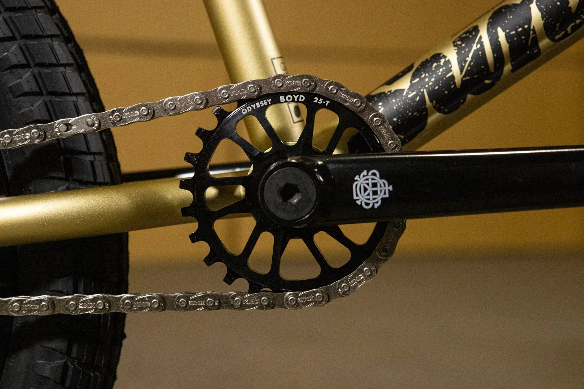 Gros plan d'un plateau Odyssey Boyd 25T et chaîne sur un cadre de vélo BMX doré.