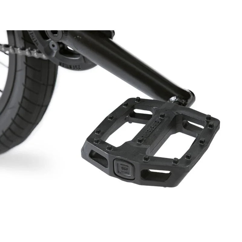Pédale BMX noire robuste avec crampons, fixée sur cadre de vélo, idéale pour tricks et freestyle