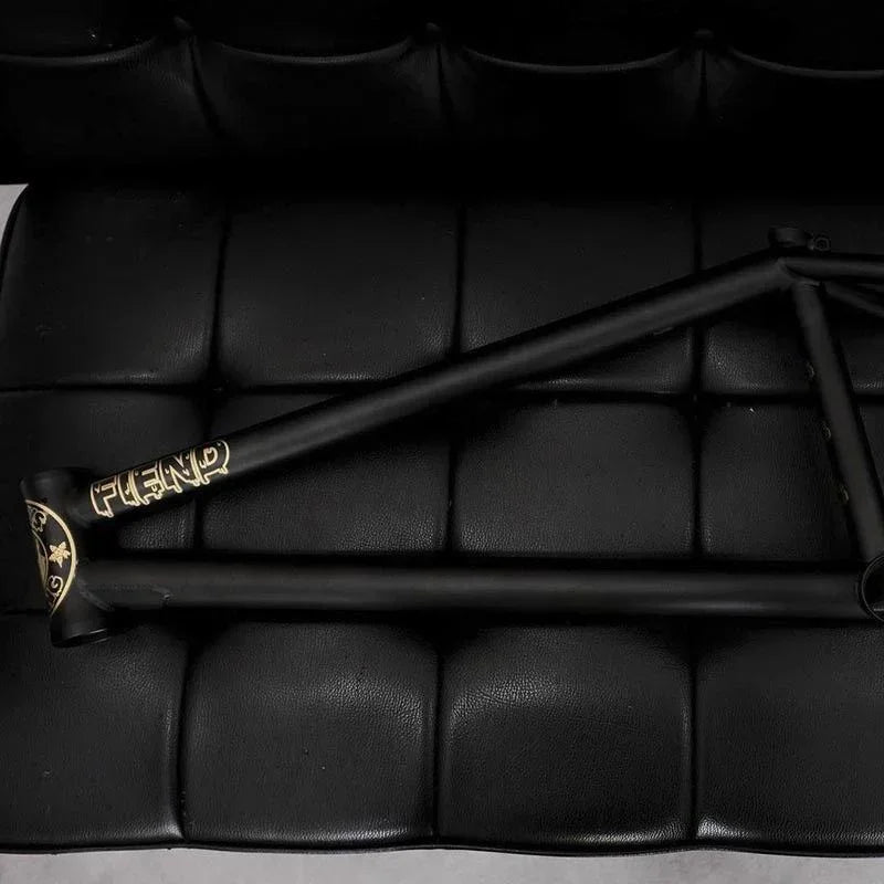 Matte black BMX bike frame with gold accents on a black padded surface