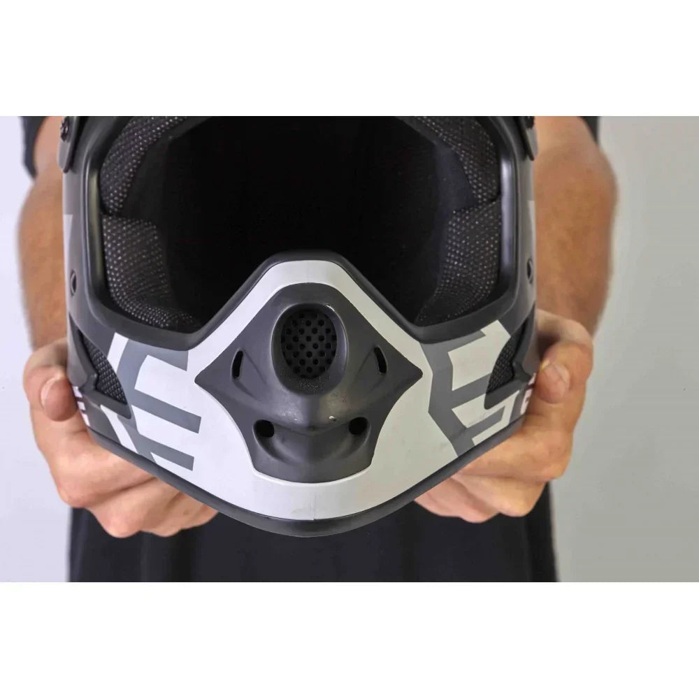 Vue de face d'un casque de BMX intégral gris et noir tenu par deux mains.