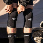 Person wearing black BMX knee pads outdoors next to a bicycle wheel