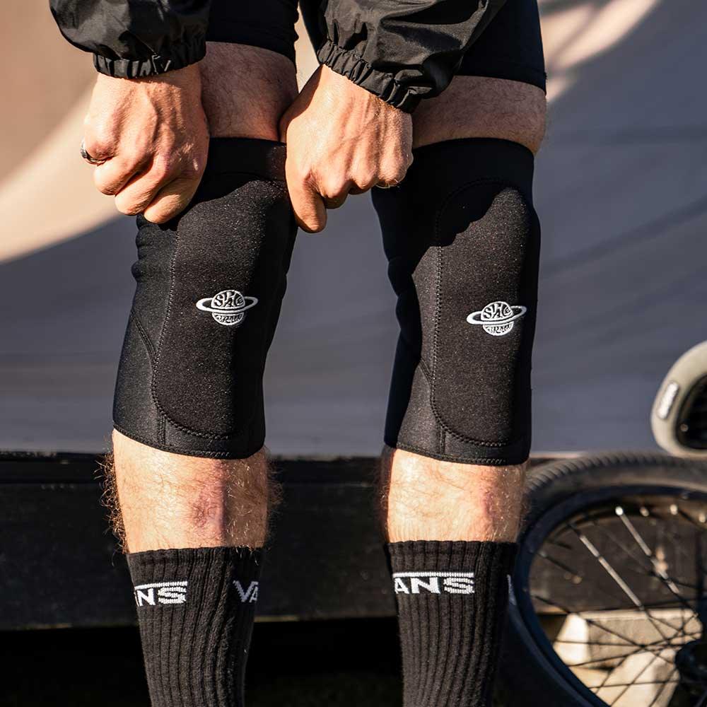 Person wearing black BMX knee pads outdoors next to a bicycle wheel