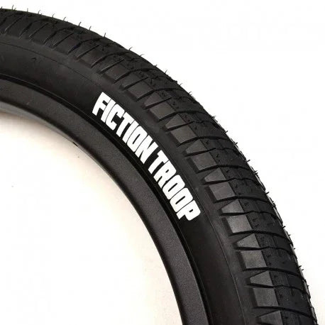 Close-up of black BMX tire with 'Fiction Troop' logo and textured tread pattern.