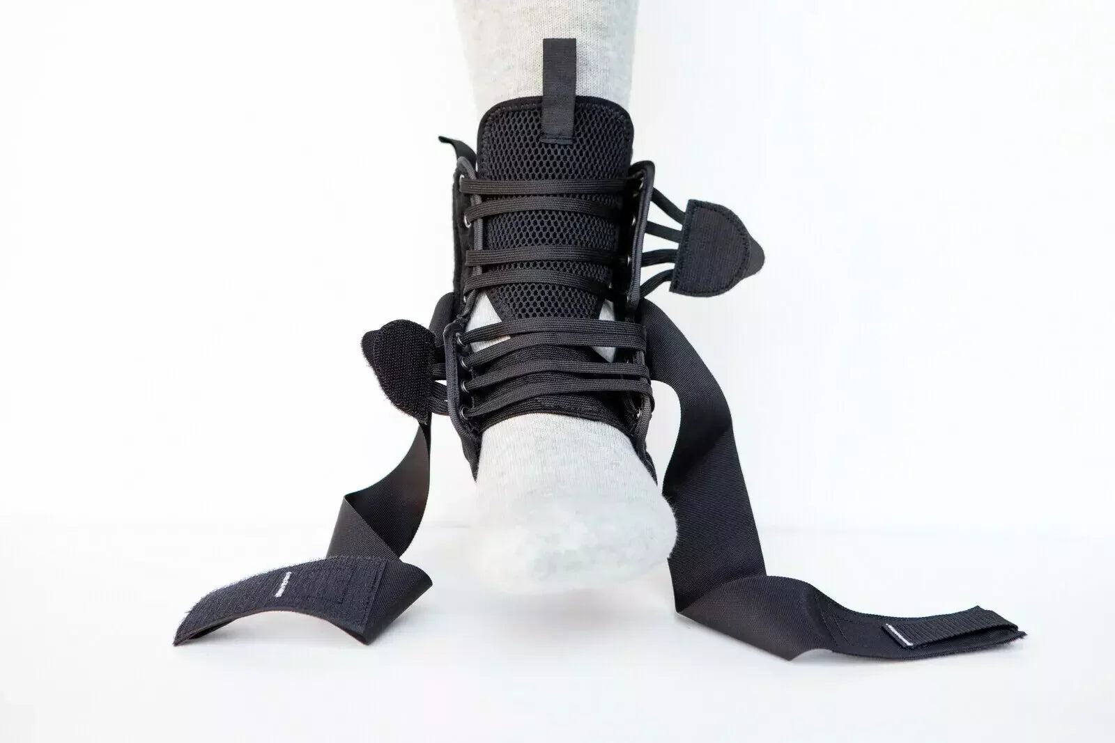 Black BMX ankle brace with adjustable straps on foot, mesh padding, and secure laces.