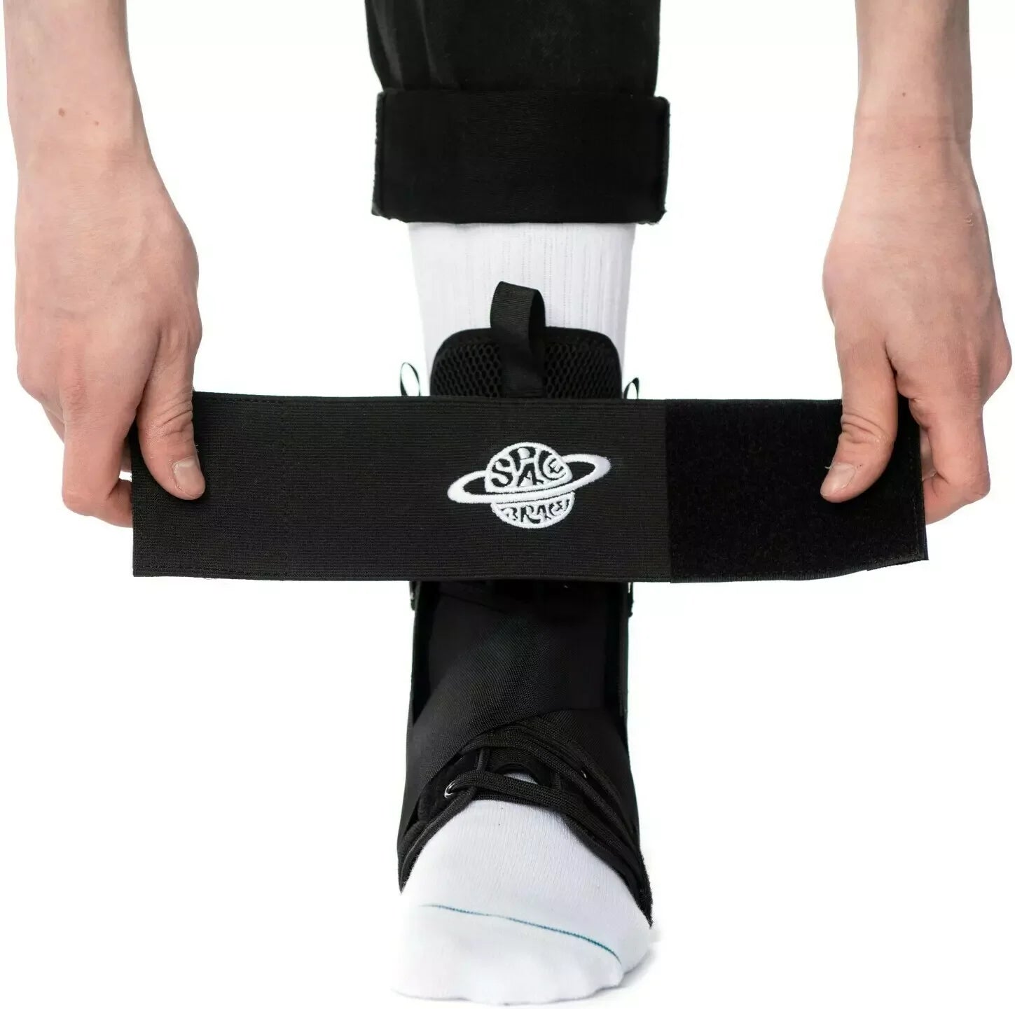 Person fitting a black ankle support brace with adjustable strap over a white sock