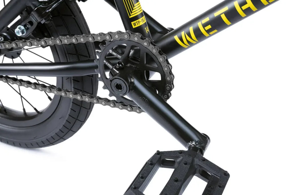 Détail de cadre BMX noir avec chaîne, pédalier et pneu, graphisme jaune vif pour freestyle