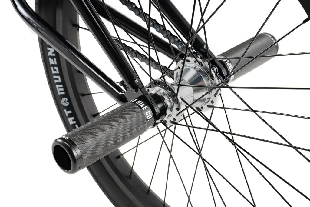 Détail de roue BMX noire avec pneu Mugen, moyeu chromé et poignées texturées